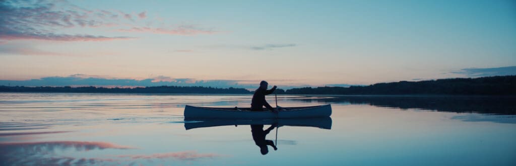Man canoeing in a traditional wooden canoe on a large lake at dawn