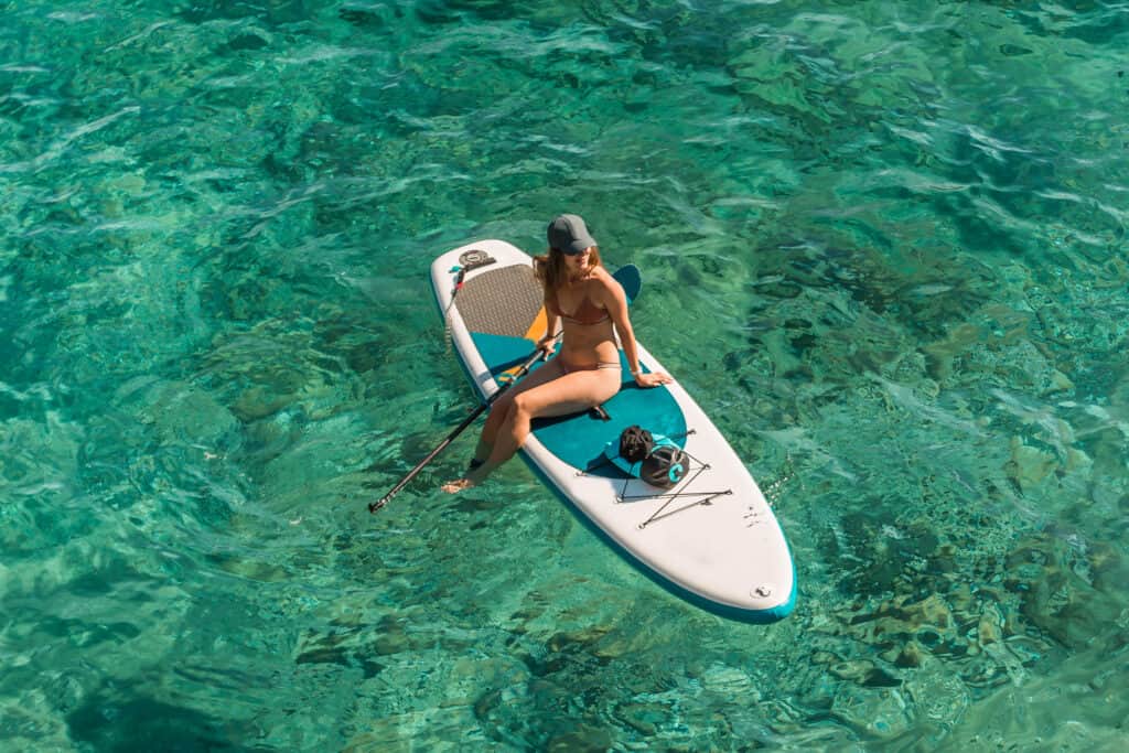 Young happy woman on SUP stand up paddle boards in turquoise water on warm summer day